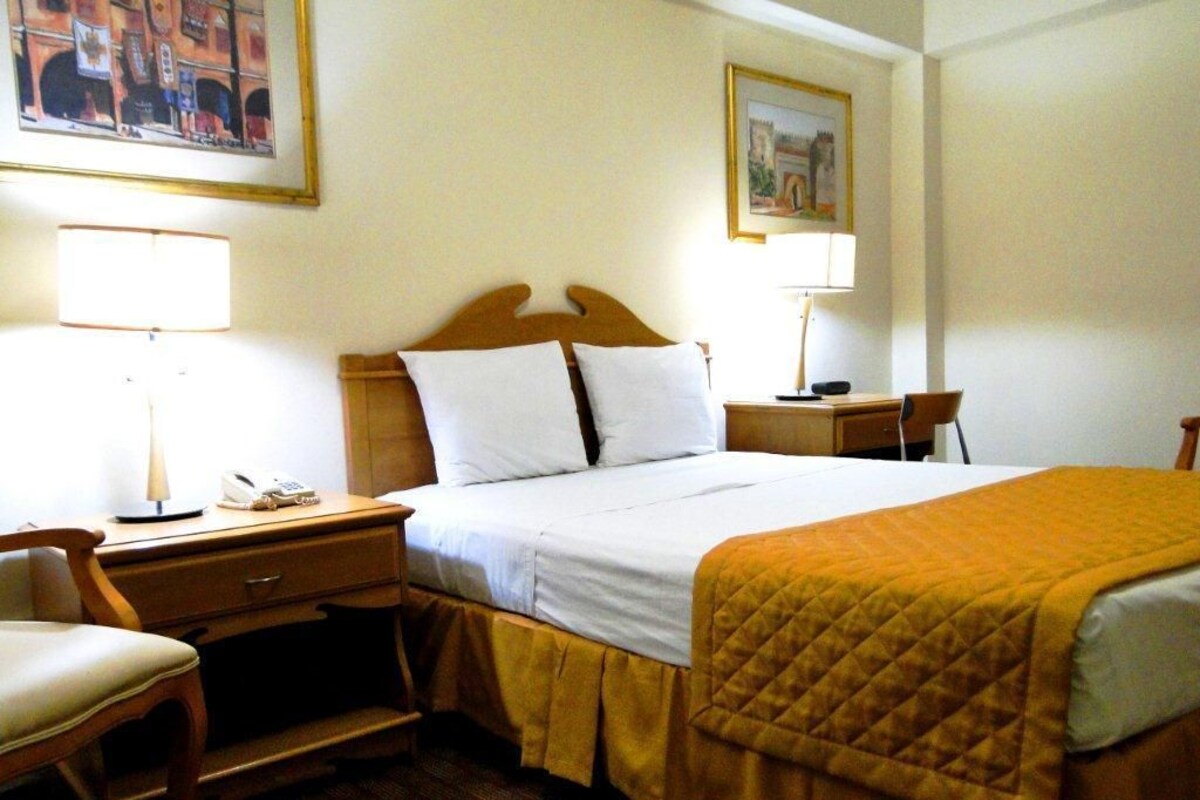 Una habitación de hotel con una cama, mesitas de noche, una silla y un escritorio.
