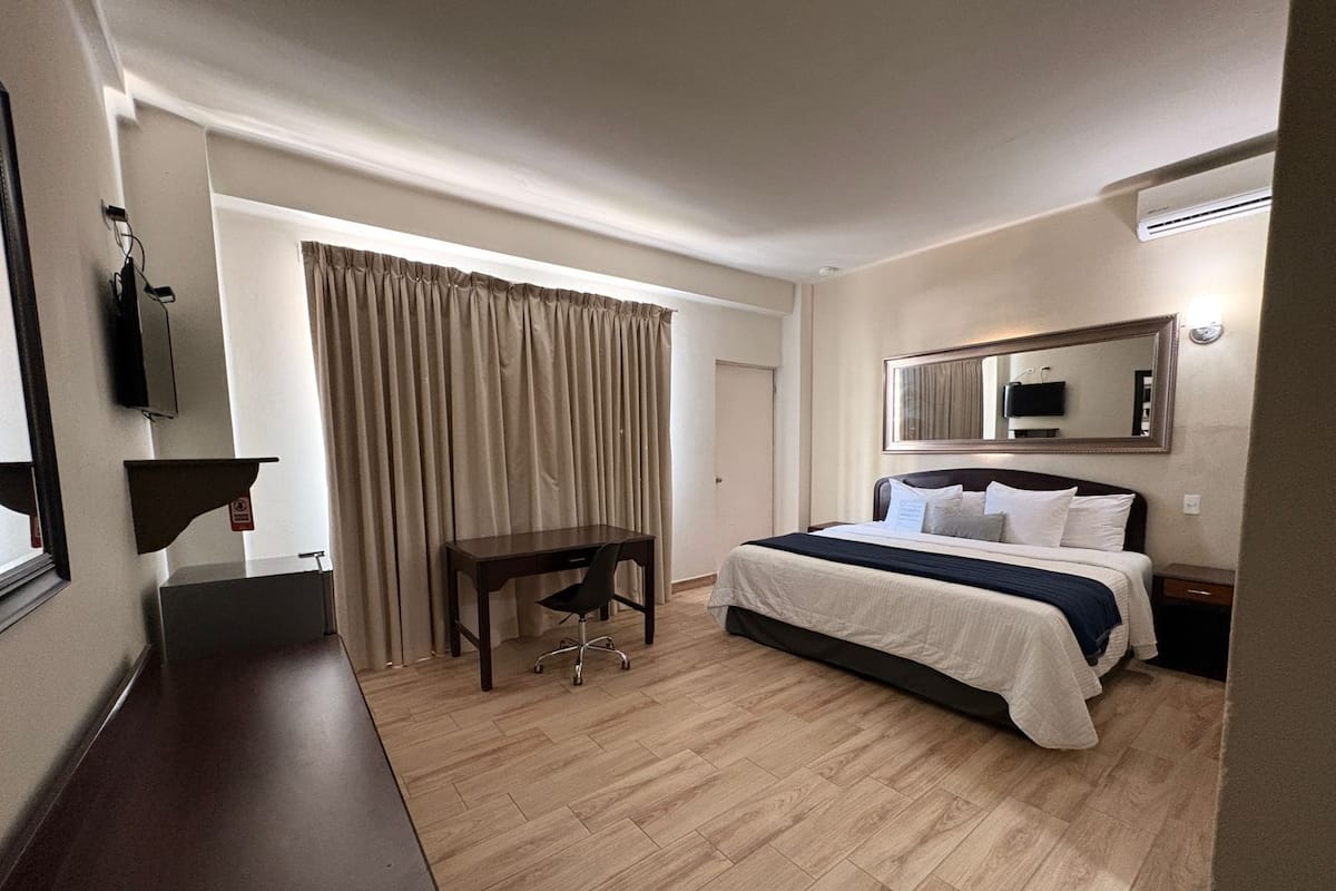 Una habitación de hotel con cama, escritorio, silla, televisión y espejo.