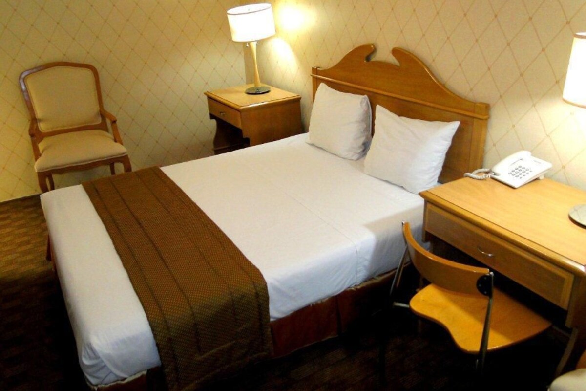 Una habitación de hotel con cama, mesita de noche, lámpara, silla y teléfono.