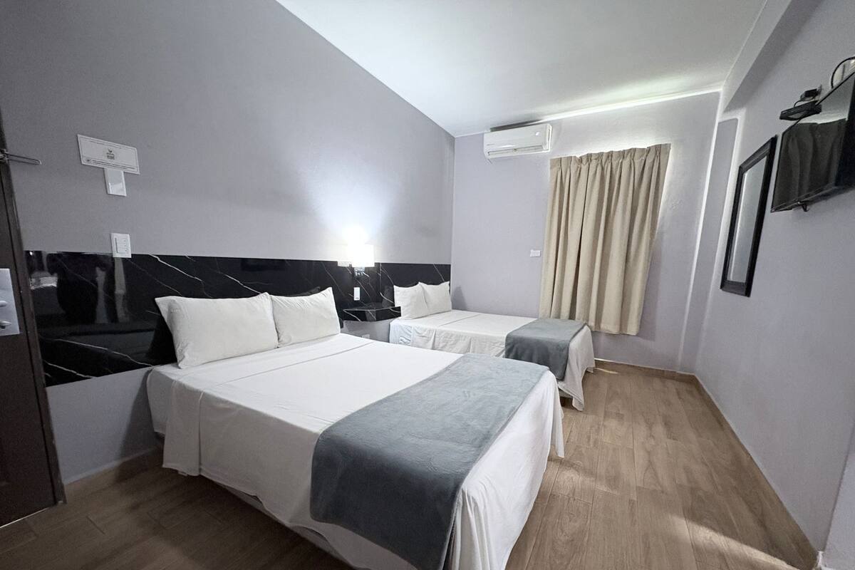 Una habitación de hotel con dos camas, un televisor de pantalla plana, un equipo de aire acondicionado y una ventana con cortinas.