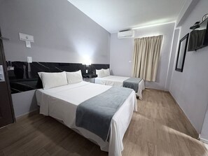 Una habitación de hotel con dos camas, un televisor de pantalla plana, un equipo de aire acondicionado y una ventana con cortinas.