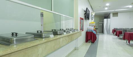 A buffet area with multiple food dispensers, a television mounted on the wall, and tables with red tablecloths.