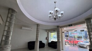 A lobby with a chandelier, columns, a black sofa, and a view of the outside. - Hotel Plaza del Arco Express (Monterrey)