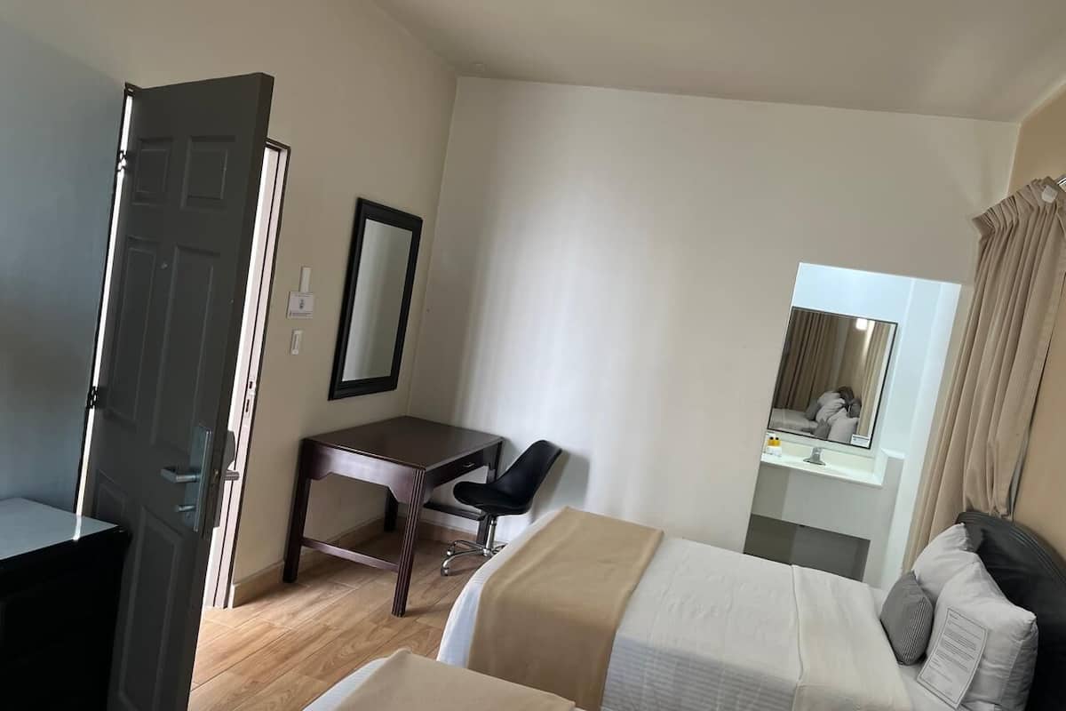 Una habitación de hotel con escritorio, dos camas, una silla, un espejo y una puerta.