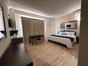 Une chambre d’hôtel avec un lit, un bureau, une chaise et une grande fenêtre avec des rideaux.