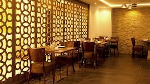 A restaurant with wooden tables and chairs, a decorative wall with circular patterns, and a stone wall in the background. - Sofi Hotel (Oran)