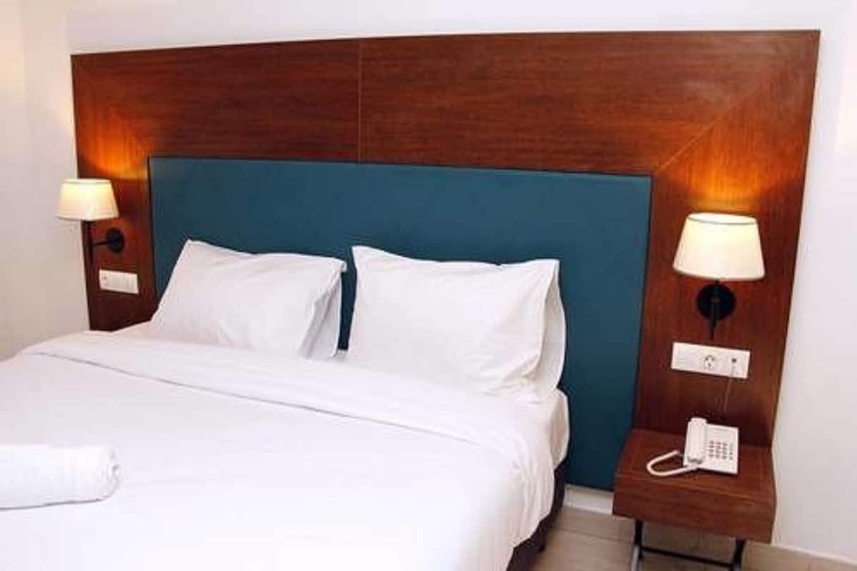 A hotel room with a large bed, a wooden headboard, two bedside lamps, and a telephone on the nightstand.