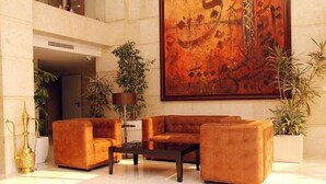 A lobby with a large abstract painting, a sofa set, a coffee table, and potted plants. - Sofi Hotel (Oran)