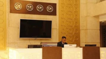 A conference room with a large flat-screen TV mounted on the wall, a podium, and a person seated behind it.