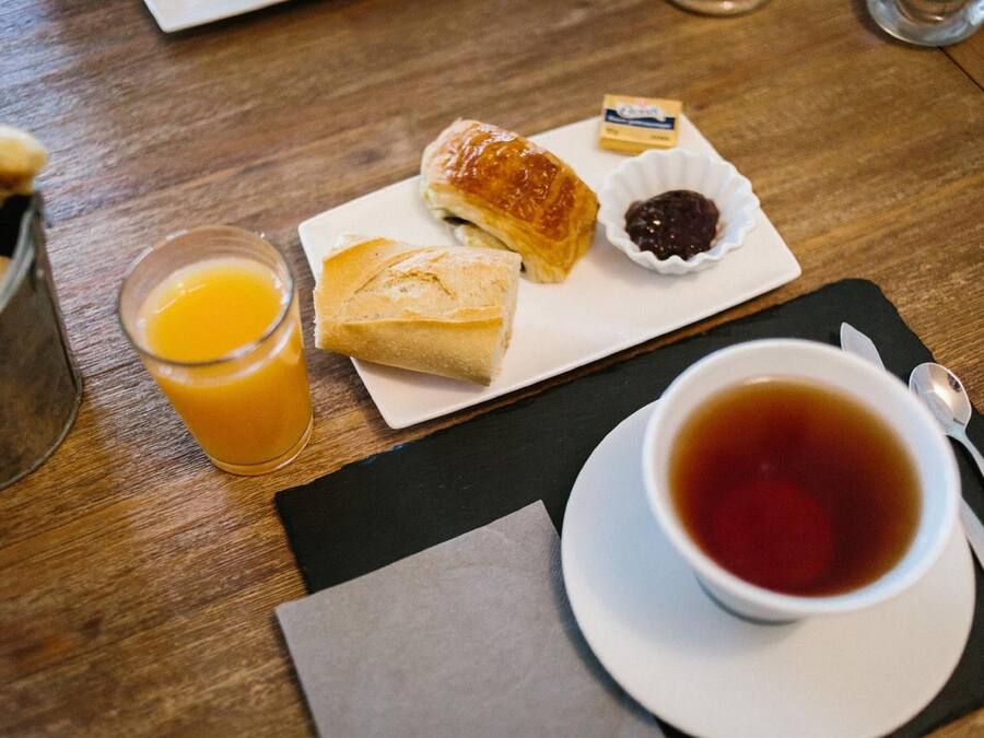 Un desayuno con bollos, un vaso de zumo de naranja y una taza de té sobre una mesa de madera.