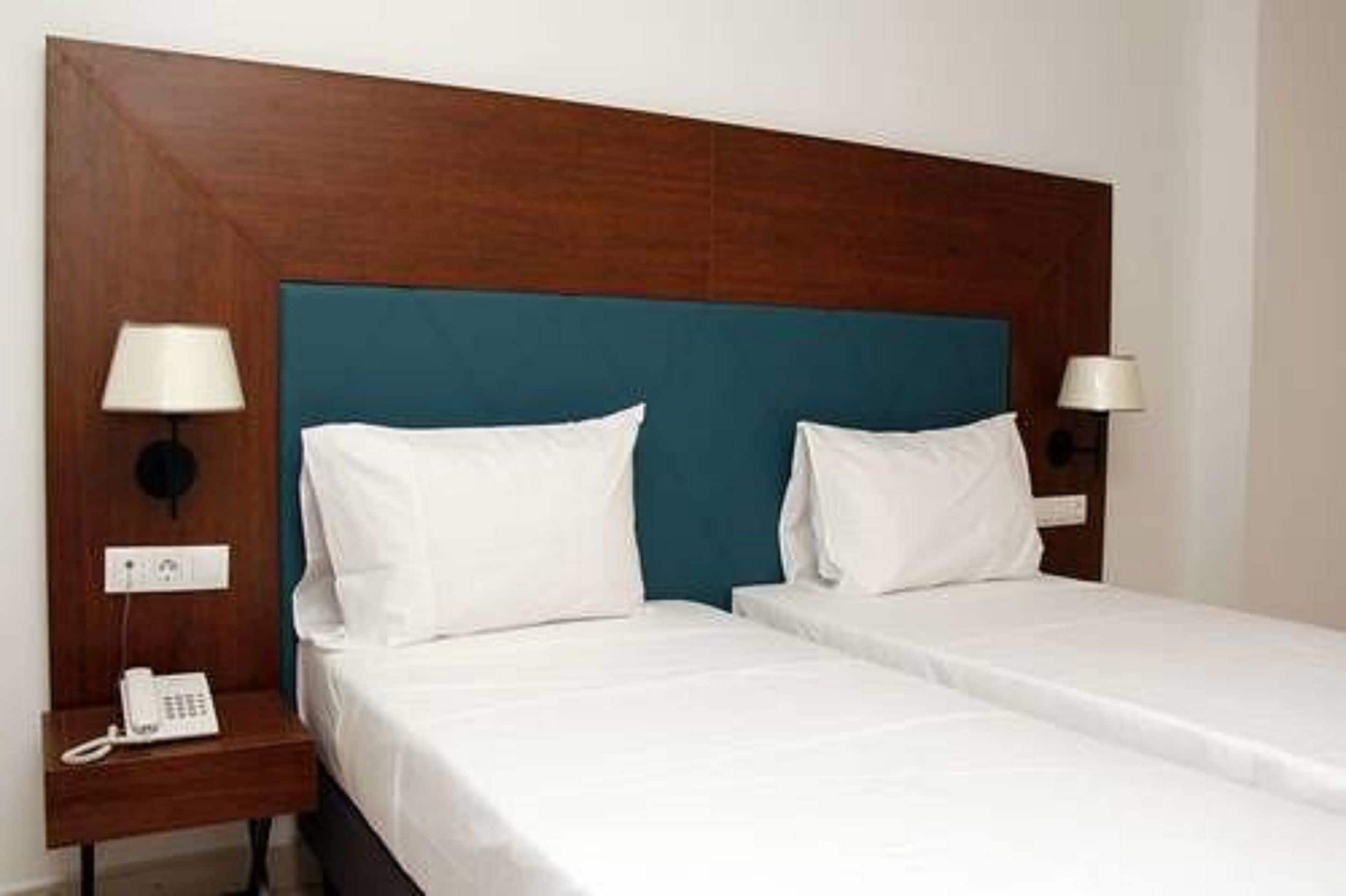 Una habitación de hotel con dos camas individuales, un cabecero de madera, lámparas de noche y un teléfono en una mesita.