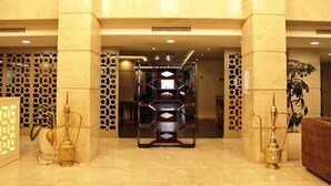 A lobby with a central staircase, decorative panels, and two brass lamps. - Sofi Hotel (Oran)