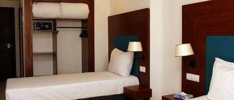 A hotel room with two single beds, each with a wooden headboard, bedside tables, and lamps.