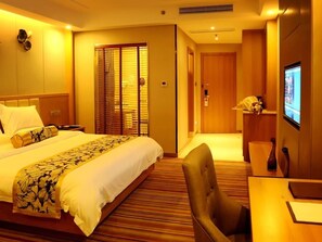A hotel room with a large bed, a desk, a chair, a television, and a sliding door.
