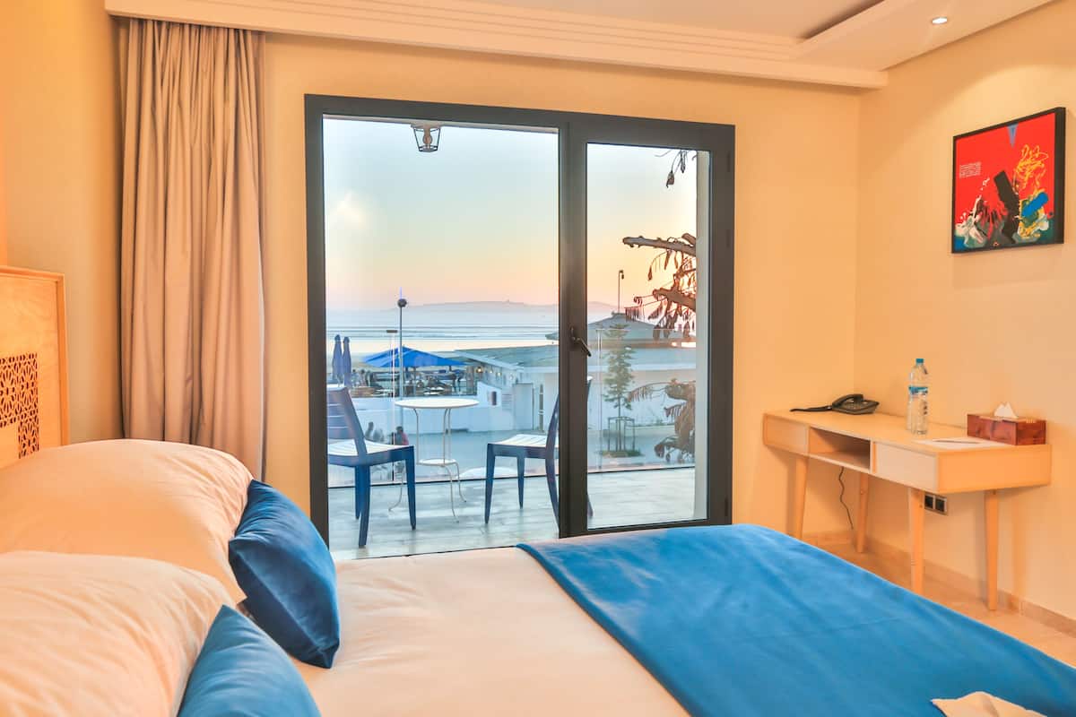 Une chambre d’hôtel équipée d’un lit, d’un bureau, d’une chaise et offrant une vue sur la mer grâce à une porte coulissante.