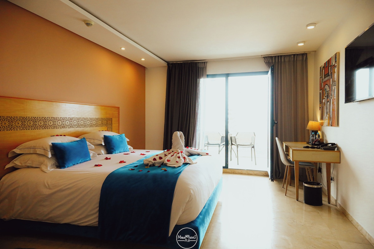 Ein Hotelzimmer mit einem großen Bett, einem Schreibtisch und Blick ins Freie.