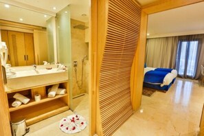 Ein Hotelzimmer mit einem Holznäpfchen, einem großen Spiegel, einer Duschkabine und einem Bett mit blauer Bettdecke.