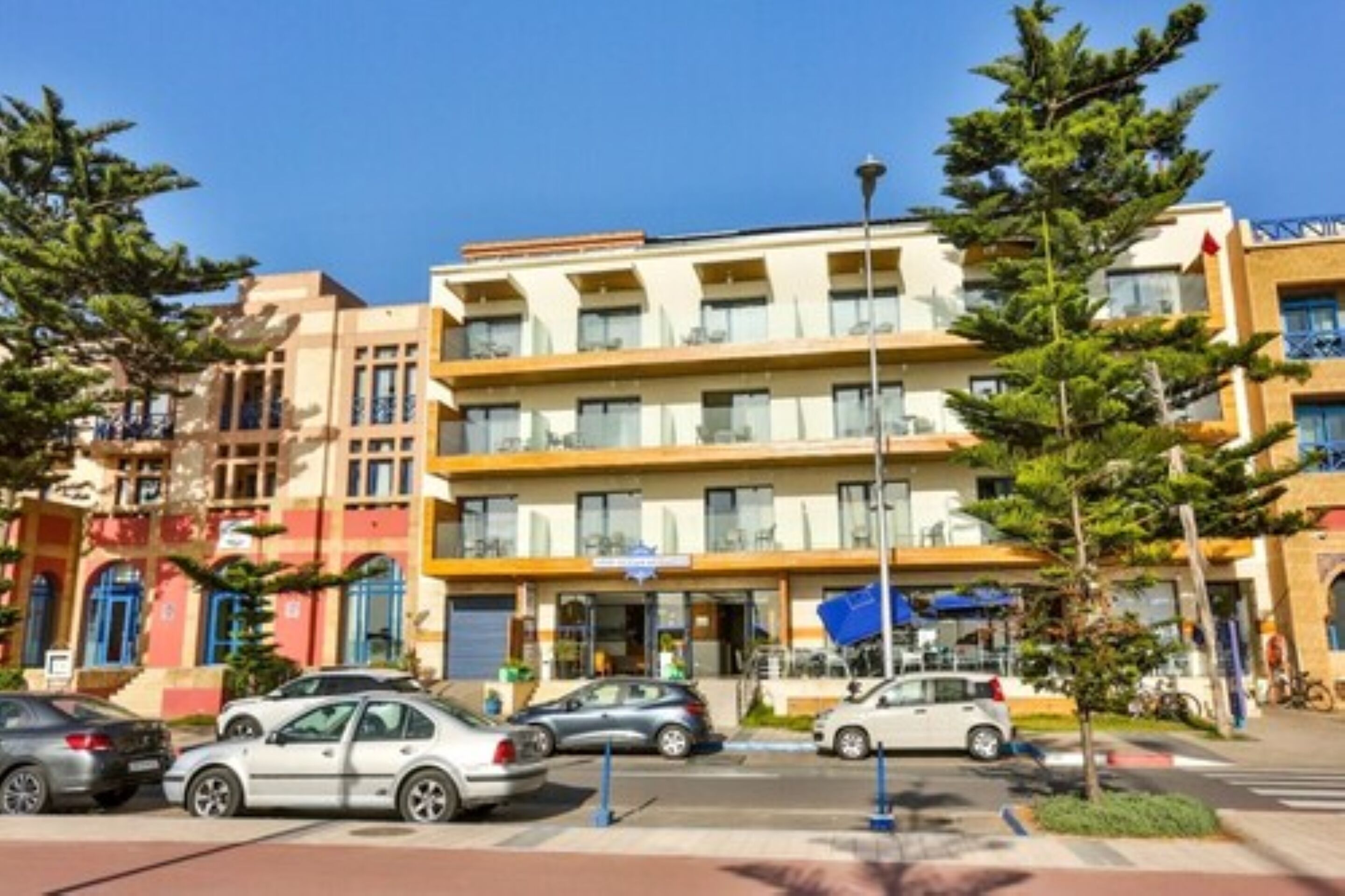 A multi-story hotel with a central entrance, parking lot, and surrounding trees.