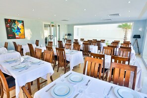 A dining area with multiple tables set for guests, featuring white tablecloths and wooden chairs. - Hotel Coté Océan Mogador (Essaouira)