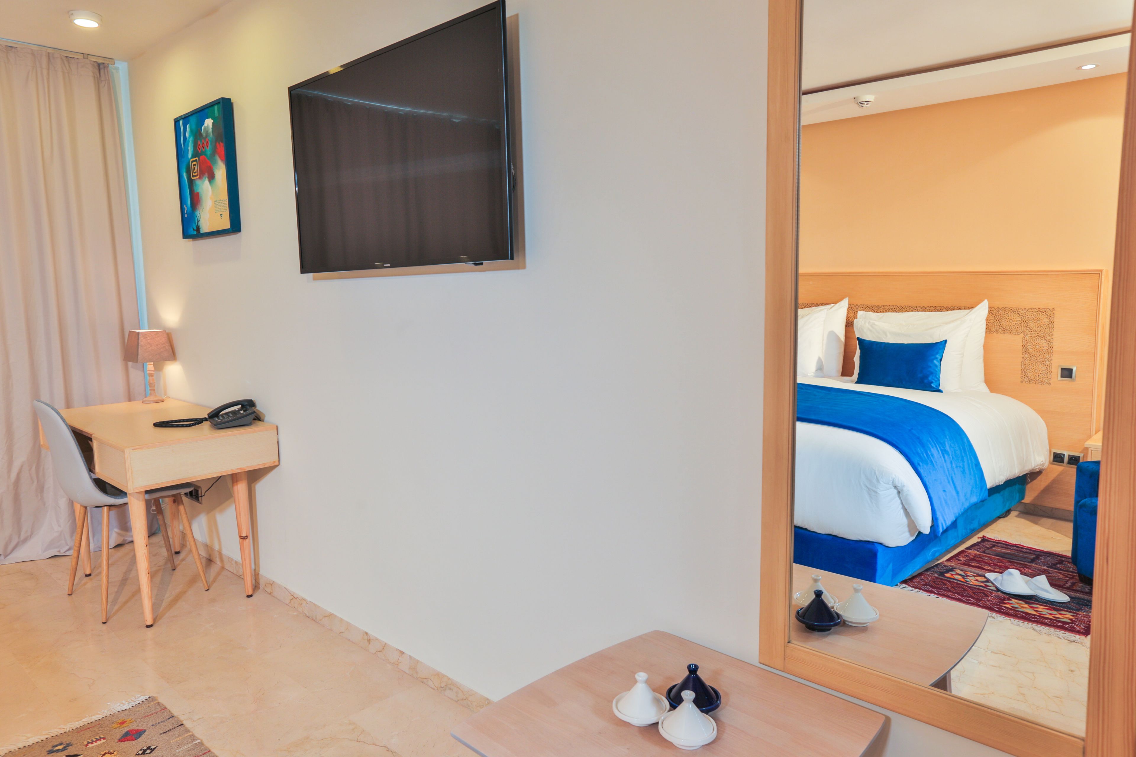 Habitación de hotel con cama, escritorio, silla, televisor y espejo.