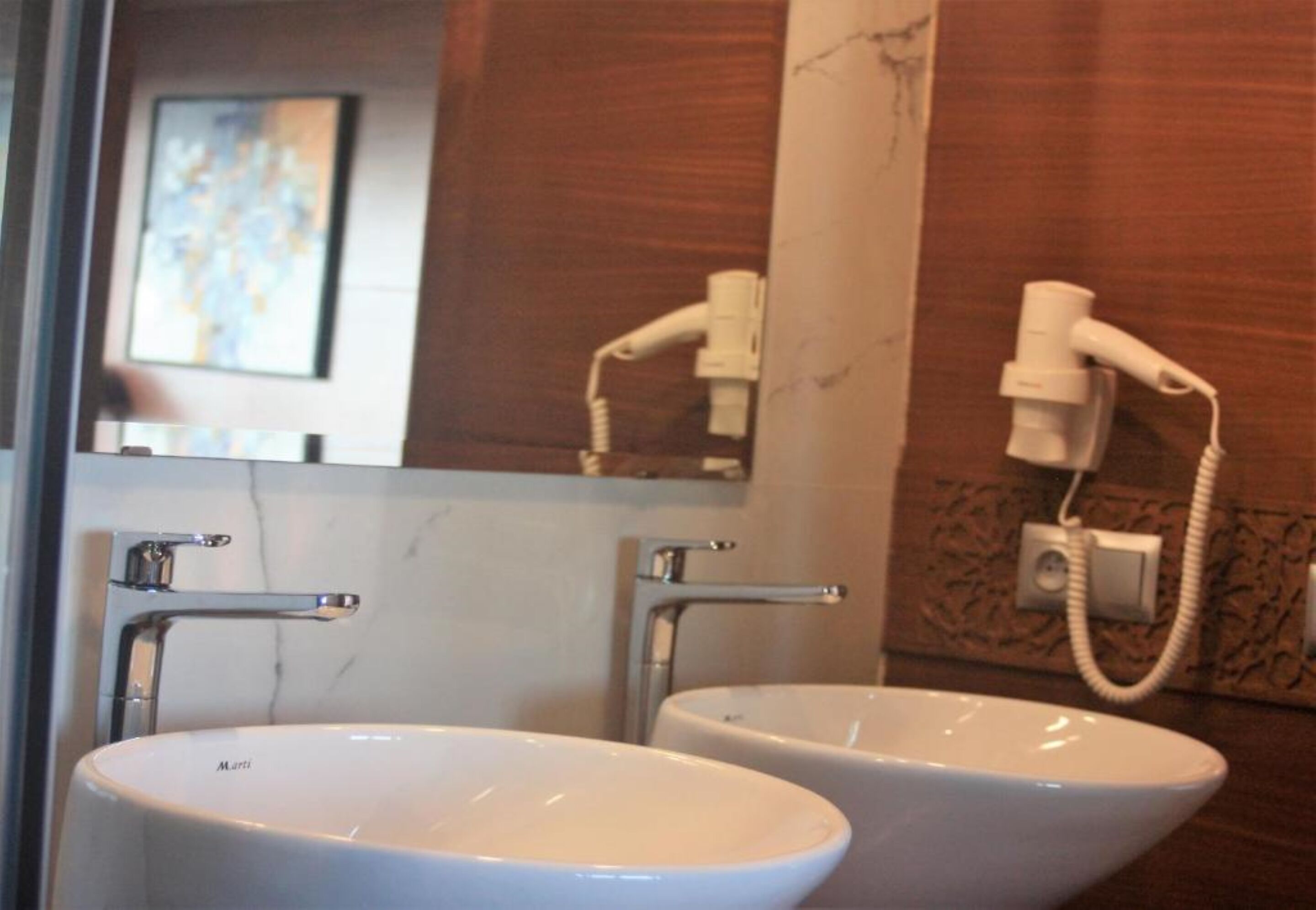 Un bagno con due lavandini bianchi, uno specchio e un asciugacapelli montato a parete.