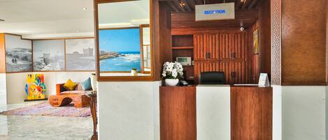 A reception area with a wooden reception desk, a large mirror, and a view of the sea through a window.