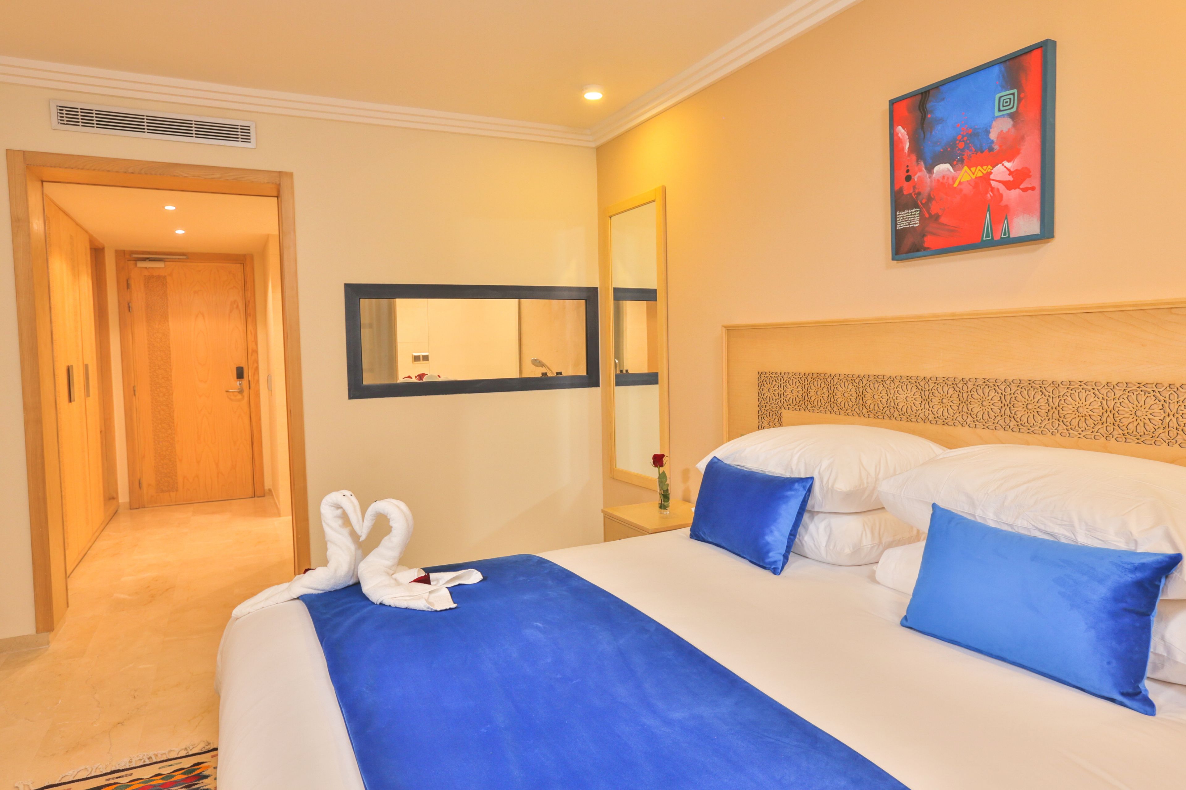 Ein Hotelzimmer mit einem großen Bett, blauer und weißer Bettwäsche, einem Gemälde an der Wand und einem Spiegel über dem Bett.