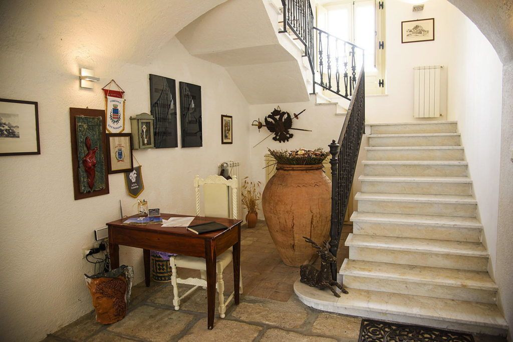 A staircase with a white railing, a wooden table with papers, and a large vase with plants.