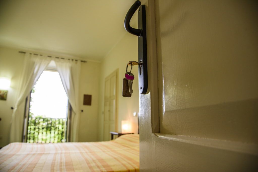 A hotel room with a bed, a door with a key lock, and a window with curtains.