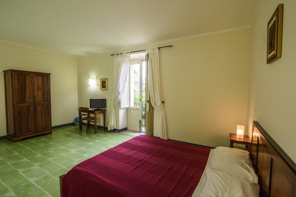 Een slaapkamer met een bed, een bureau met computer, een kledingkast en een raam met gordijnen.
