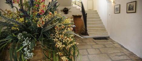 Un pasillo con un arreglo floral grande, una escalera y un piso de piedra.