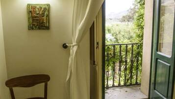 A room with a chair, a wall-mounted light, a door leading to a balcony, and a view of greenery outside.