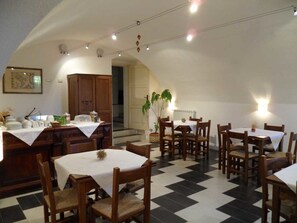 Un comedor con mesas y sillas, una cocina con armarios y una planta.