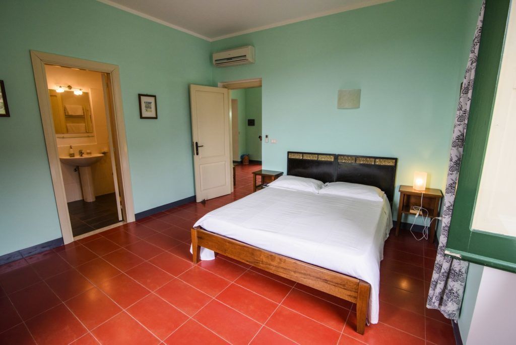 Un dormitorio con una cama de madera, un espejo, un lavamanos y una puerta que da a otra habitación.