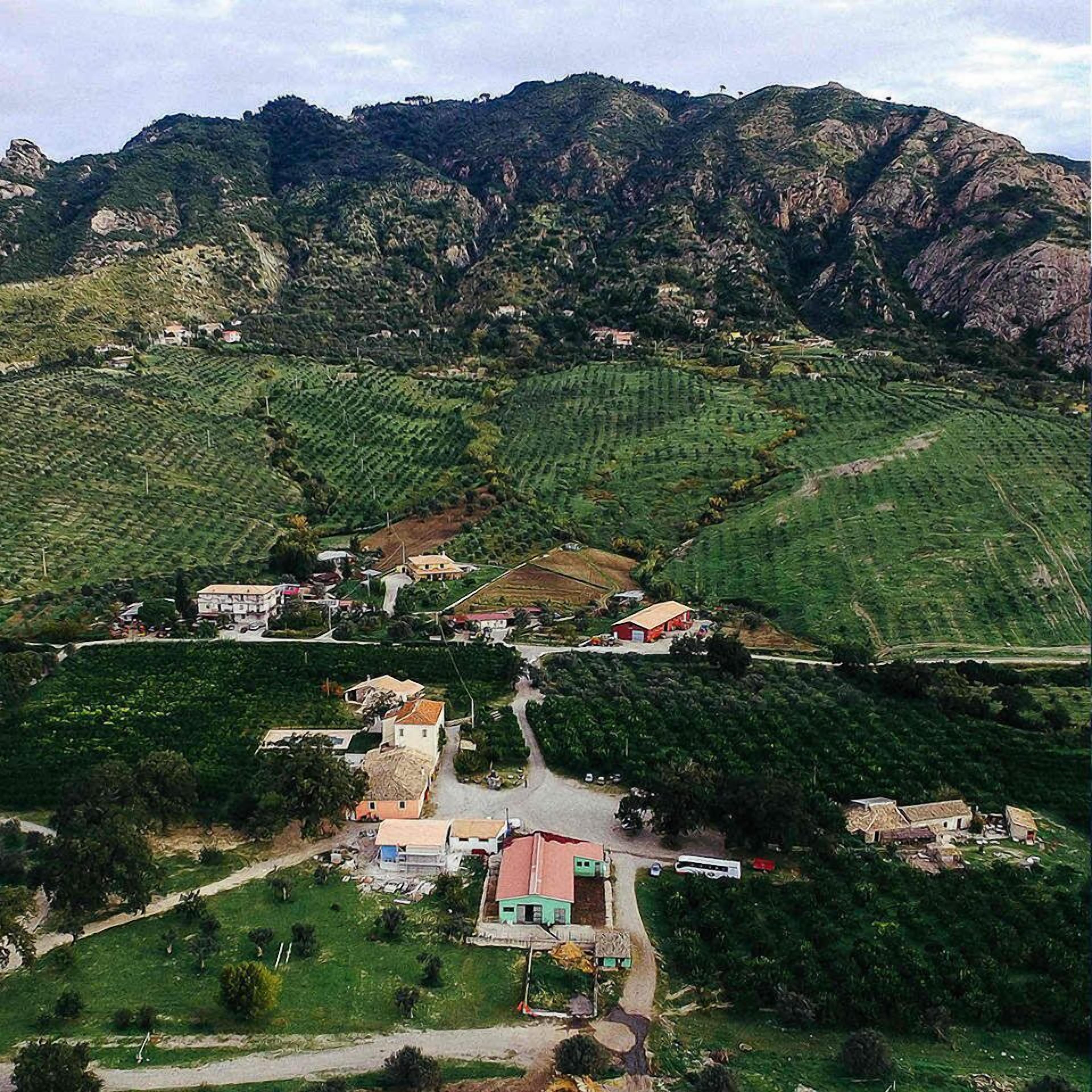 Paisaje rural con campos en terrazas, algunas construcciones dispersas y una cadena montañosa al fondo.