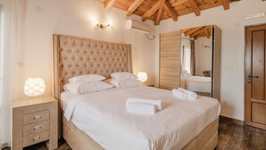 Un dormitorio con una cama grande, vigas de madera en el techo, una mesita de noche con cajones, una lámpara de noche y un espejo.