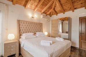 Une chambre Ă coucher avec un grand lit, des poutres apparentes en bois au plafond, une table de chevet avec des tiroirs, une lampe de chevet et un miroir.