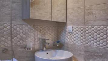 Un baño moderno con un lavamanos redondo, un espejo encima y una toalla colgada en la pared.