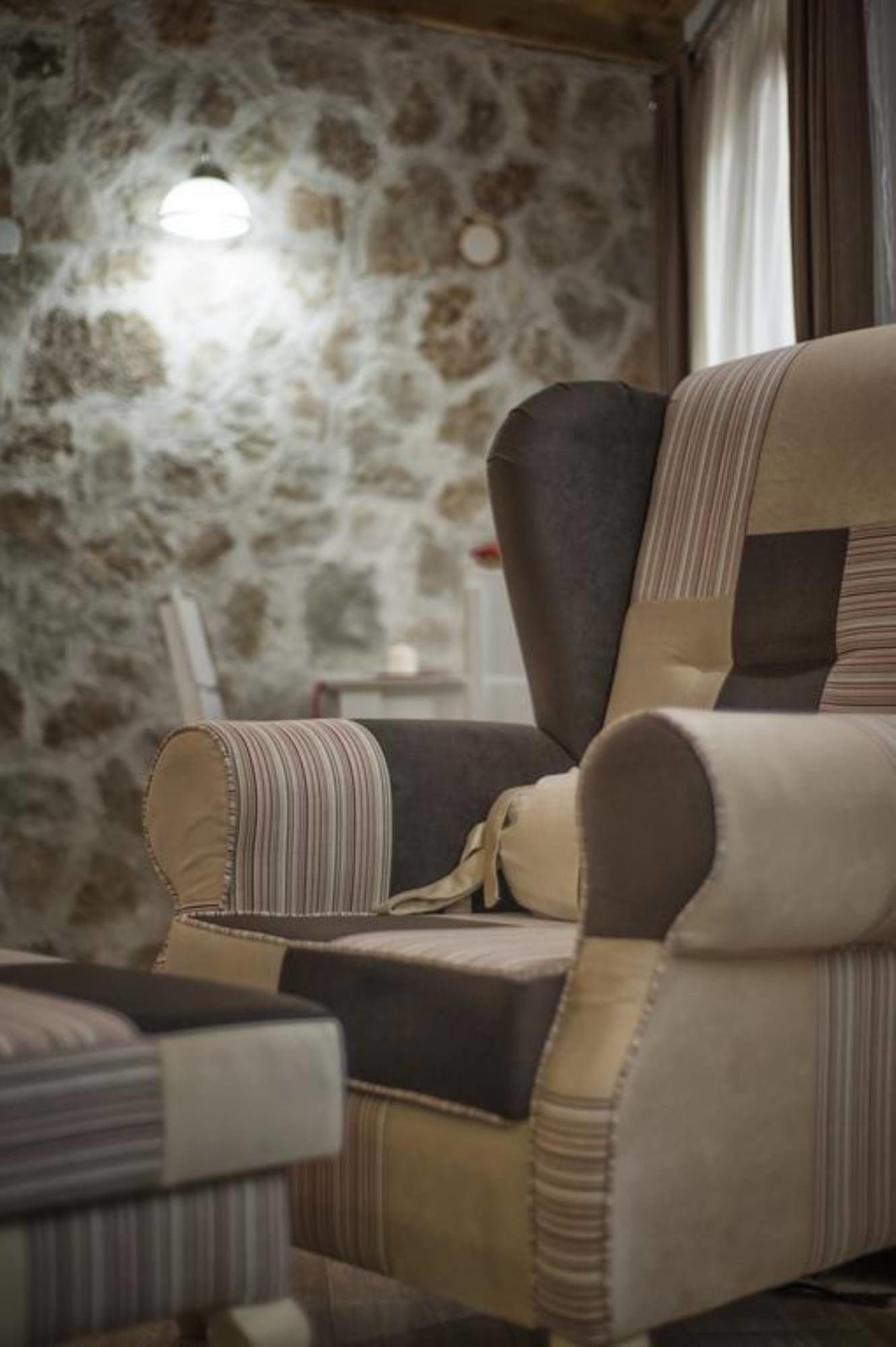 Un sillón estilo vintage con tapicería a rayas, ubicado en una habitación con pared de piedra y lámpara colgante.