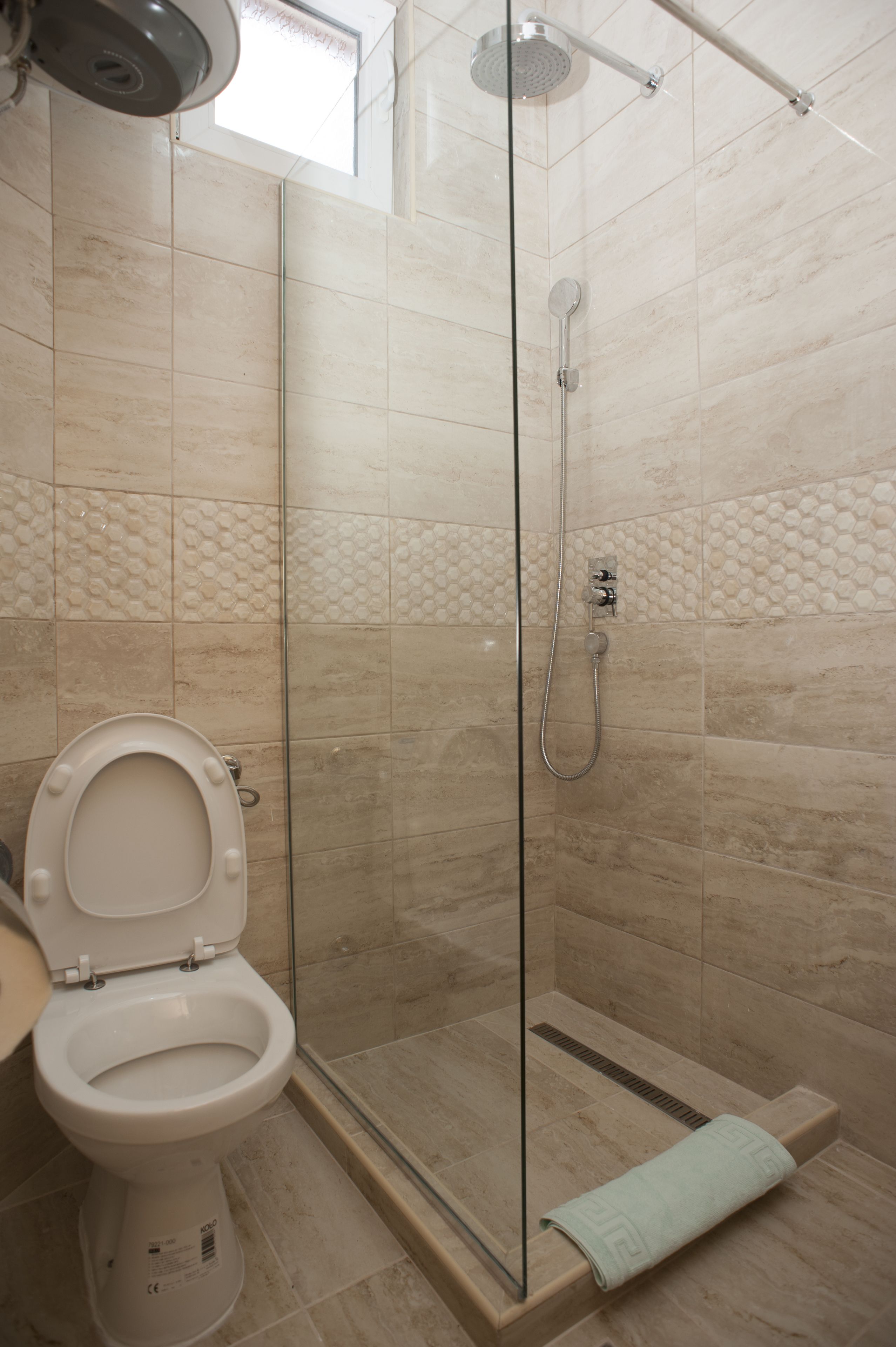 A bathroom with a glass-enclosed shower, a toilet, and a towel on the floor.