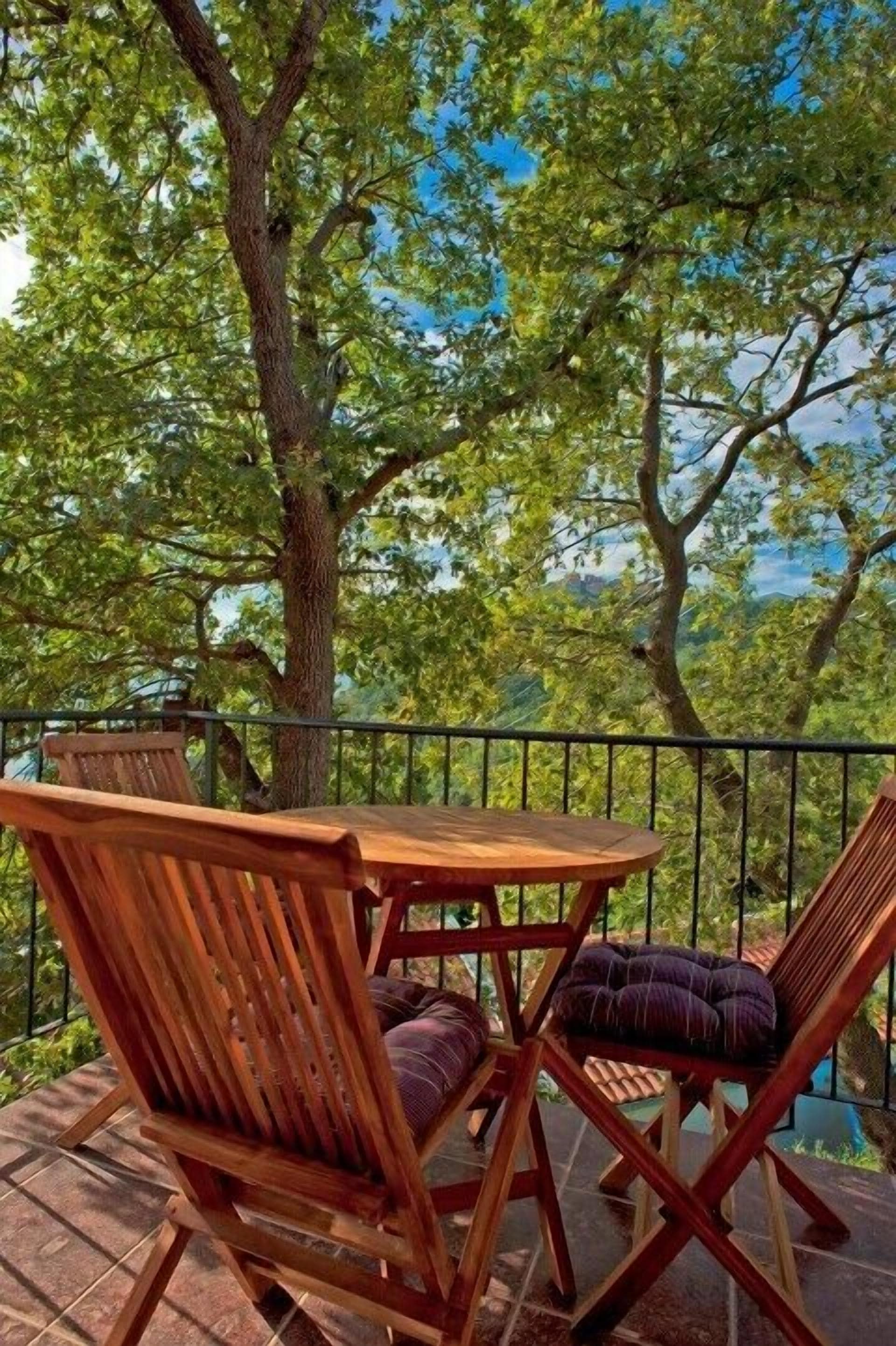 Un tavolo e sedie di legno su un balcone con vista su alberi e cielo sereno.