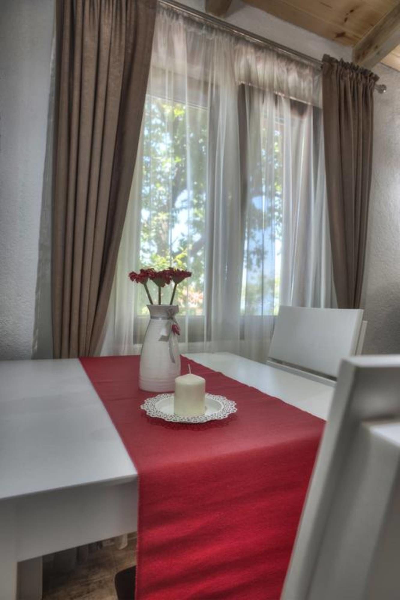A room with a table set for two, a vase with flowers, and a candle on a red tablecloth.