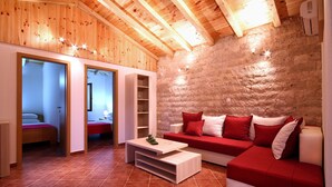 Una habitación acogedora con techo de madera, pared de piedra, sofá rojo y cama con manta roja.