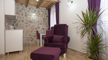 Une pièce avec un mur en pierre, un fauteuil violet, une petite table, une armoire blanche et une plante en pot.