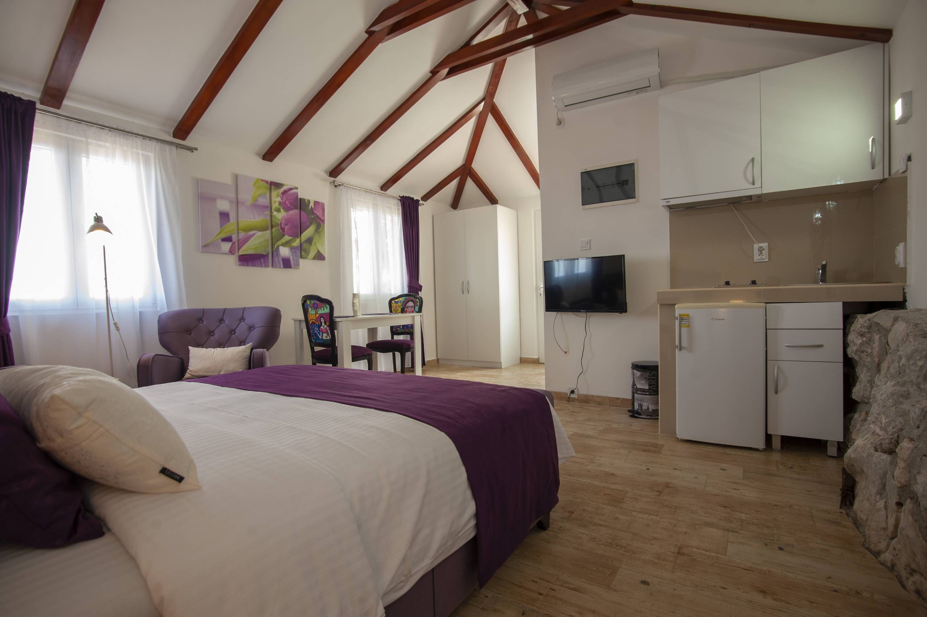 Un dormitorio con cama, escritorio, silla, televisor y kitchenette.