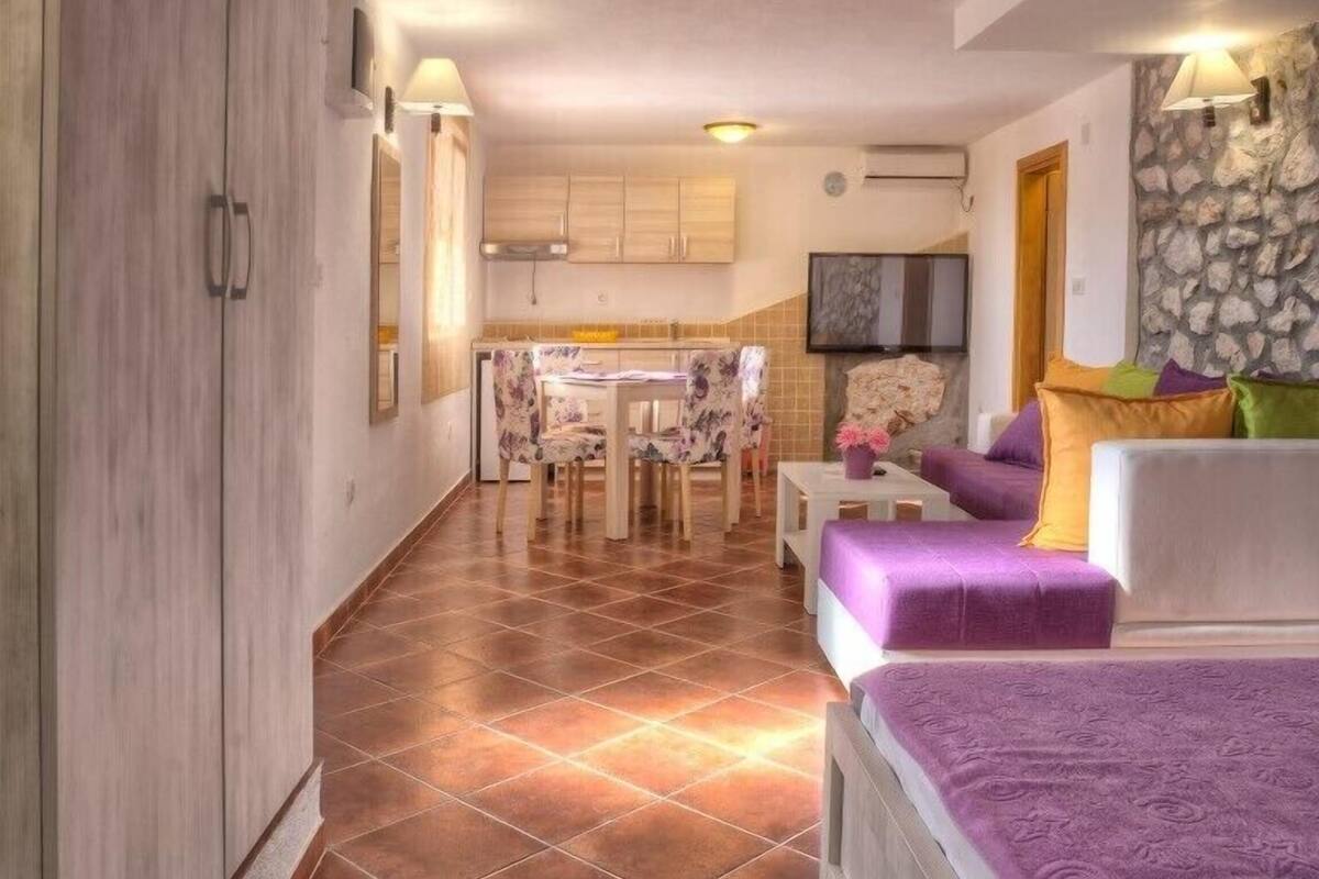 A modern apartment with a dining area, a kitchen, and a living room with a sofa and a TV.