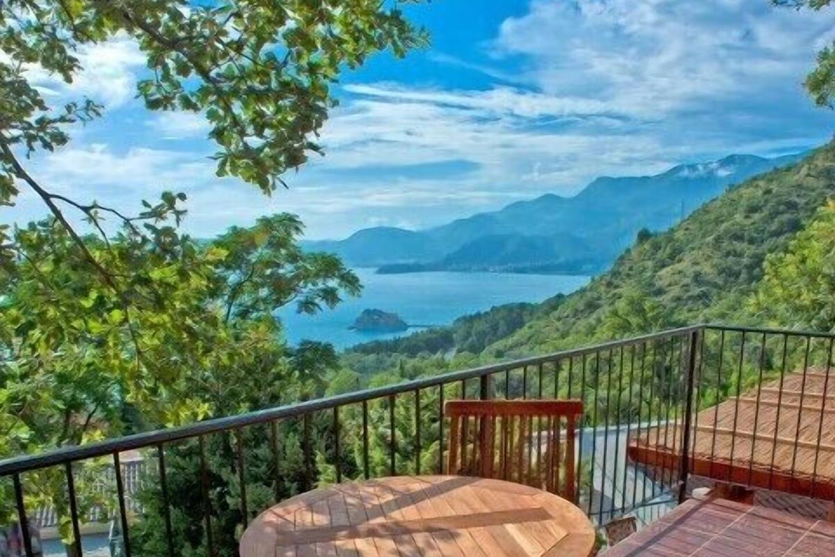 A wooden deck with a round table and two cushioned chairs, overlooking a mountainous landscape and a body of water.