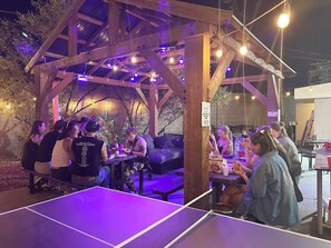 An outdoor seating area with a ping pong table, wooden pergola, and string lights. - Sin City Hostel Las Vegas (Las Vegas)