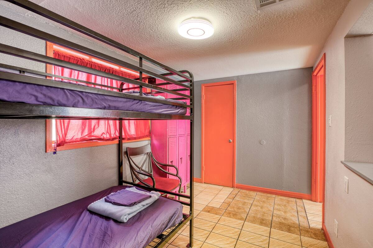 Een slaapzaal met stapelbedden, een stoel, een deur en een betegelde vloer.