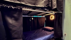 Una cama litera con colchón y almohadas, cabecera con luz y un enchufe en la pared.